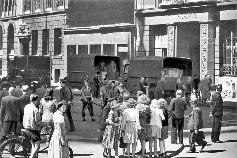 Währungsreform 1948: Unter strenger britischer Bewachung werden Lastkraftwagen mit Kisten vor dem Gebäude der Hamburger Landeszentralbank abgeladen. Die scharfe Absperrungsring um das Bankgebäude lässt vermuten, dass das neue Geld in das Bankgebäude eingeliefert wird. | Quelle/Foto: Bundesarchiv